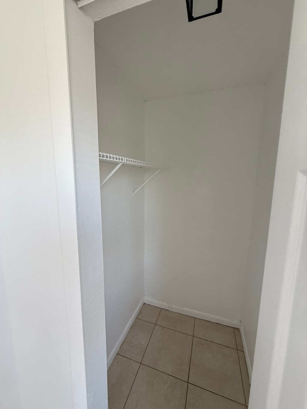 A white closet with a shelf and tiled floor.