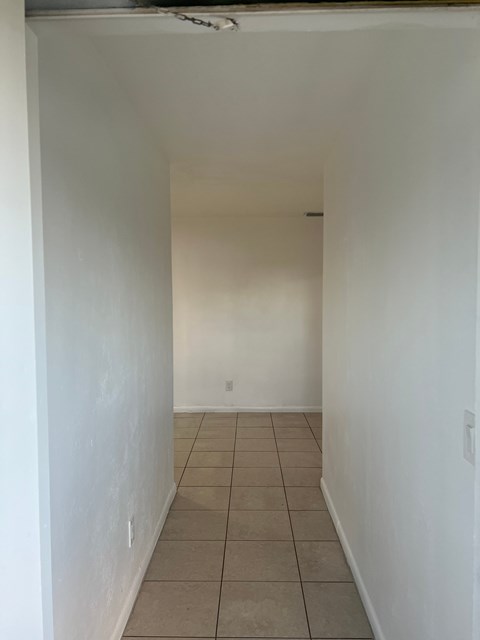 A white hallway with tiled flooring and a white door at the end.