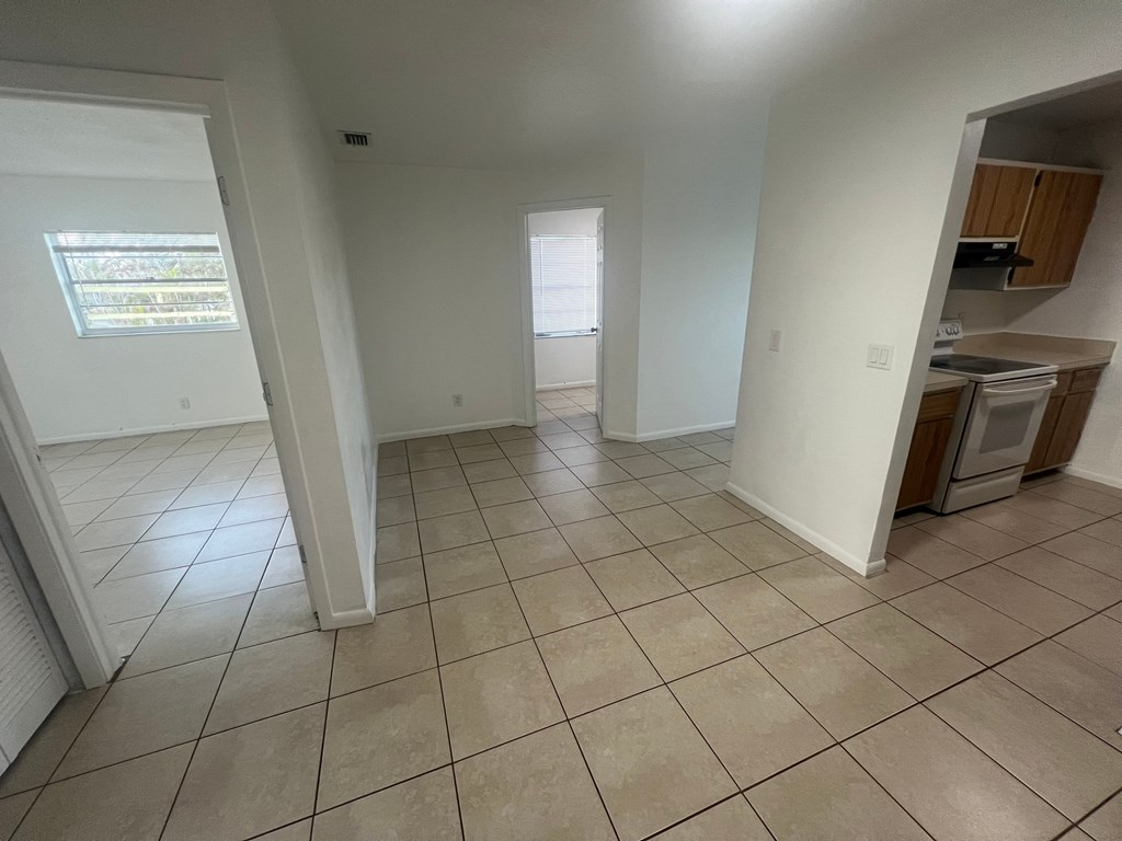 A spacious living room with tiled flooring and a kitchen area in the background.