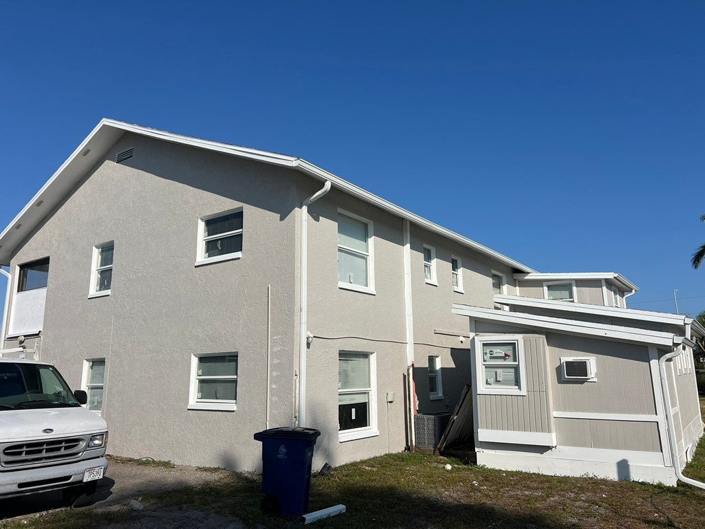 A white house with a blue trash can in front of it.