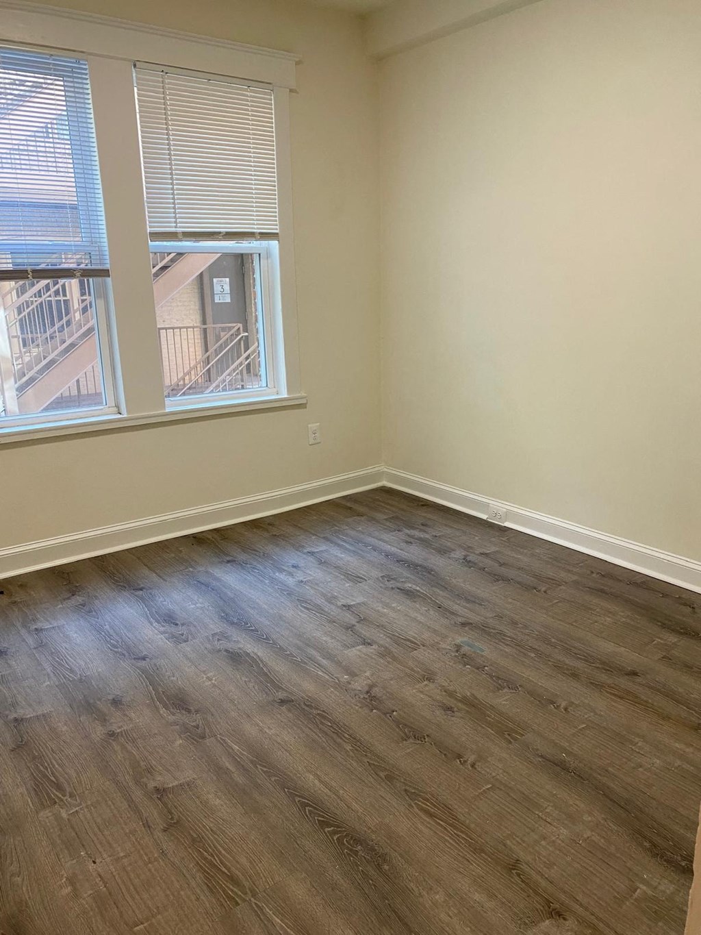 an empty room with wooden floors and two windows