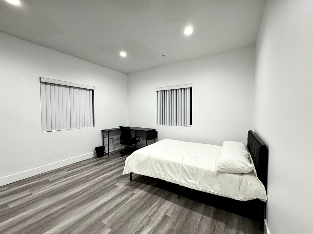 a bedroom with a bed and a desk and two windows