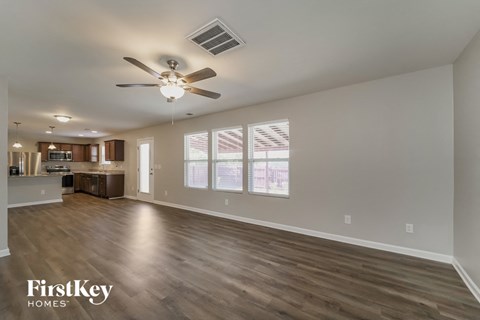 an empty living room with a ceiling fan and a kitchen