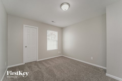 a bedroom with carpet and a white door and a window