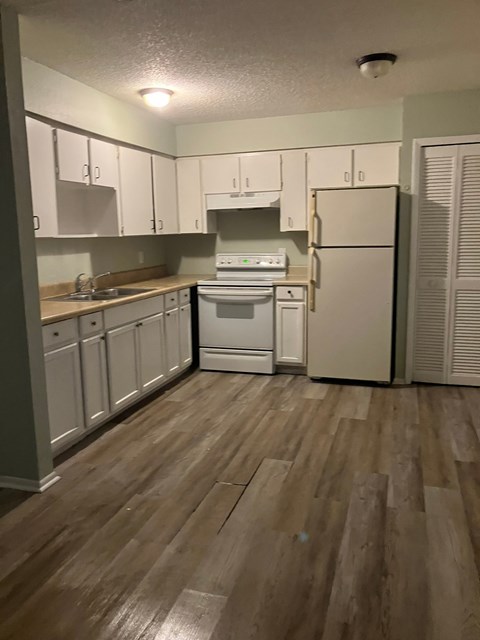 A kitchen with white appliances and wooden floors.
