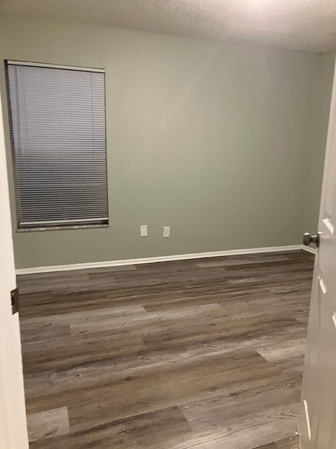 A room with a wooden floor and a window with blinds.