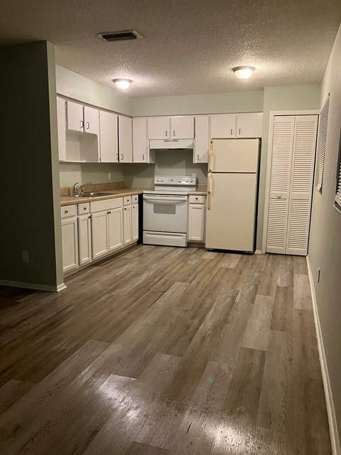A kitchen with white appliances and wooden floors.