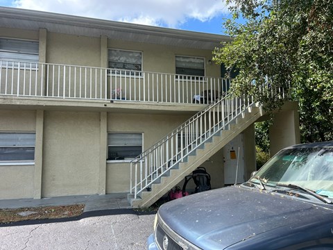 A car is parked in front of a two-story building with a balcony.