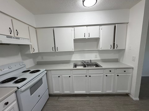 A white kitchen with a stove, sink, and cabinets.