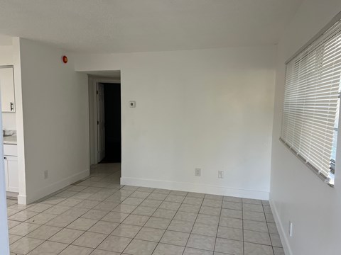 A room with white walls and a tiled floor with a doorway leading to another room.