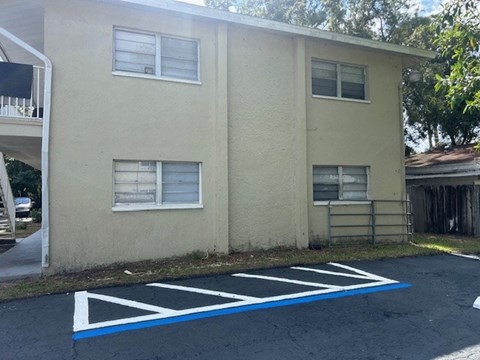 A parking lot in front of a beige building with a white railing on the left.