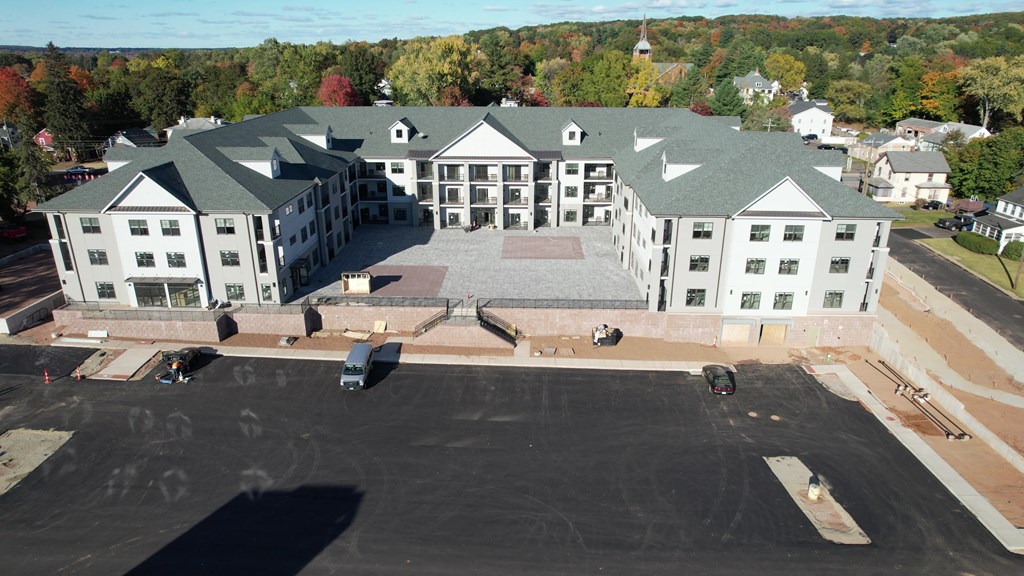 A large white building with a green roof is surrounded by a parking lot.