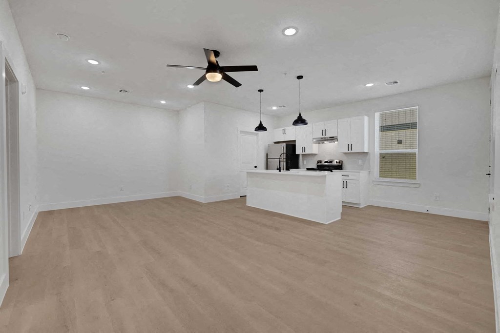an empty living room with a kitchen and a ceiling fan