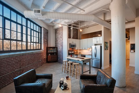 A living room with black leather couches and a kitchen in the background.