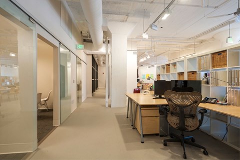 A modern office with a glass wall and a desk with a computer and chair.