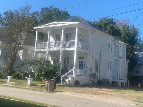 A white two-story house with a porch and a tree in front.