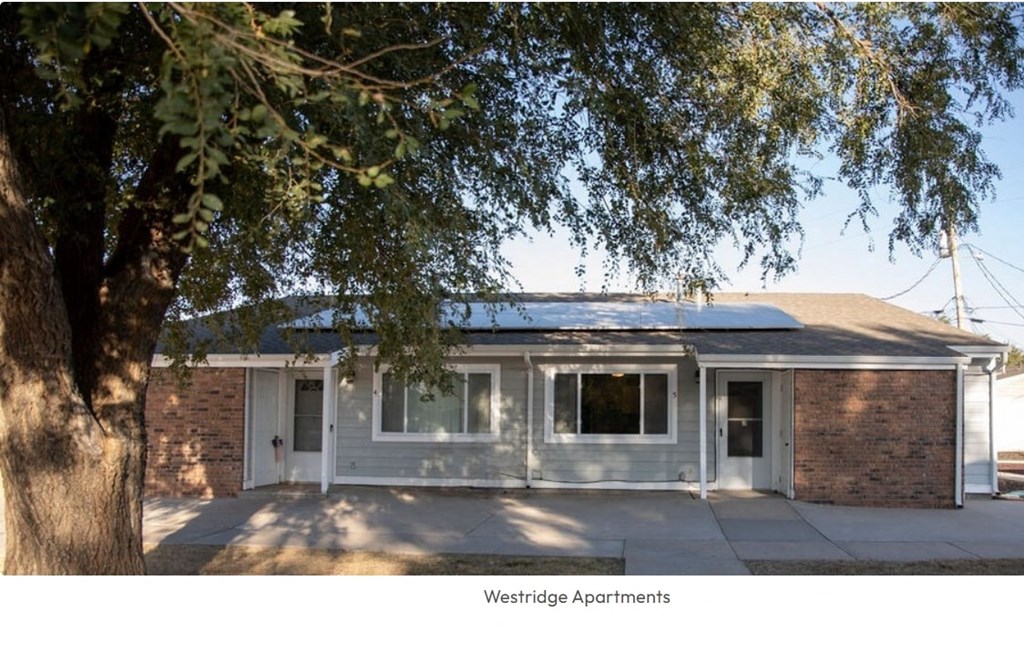 A tree is in front of a brick building with the words Westridge Apartments written below it.