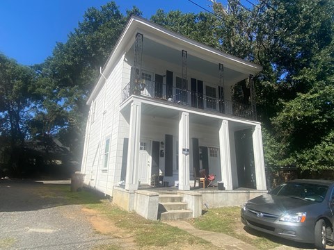 A white house with a balcony and a car parked in front.