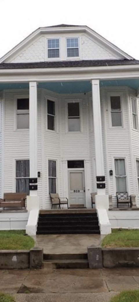 A white house with a black roof and a porch with a bench.