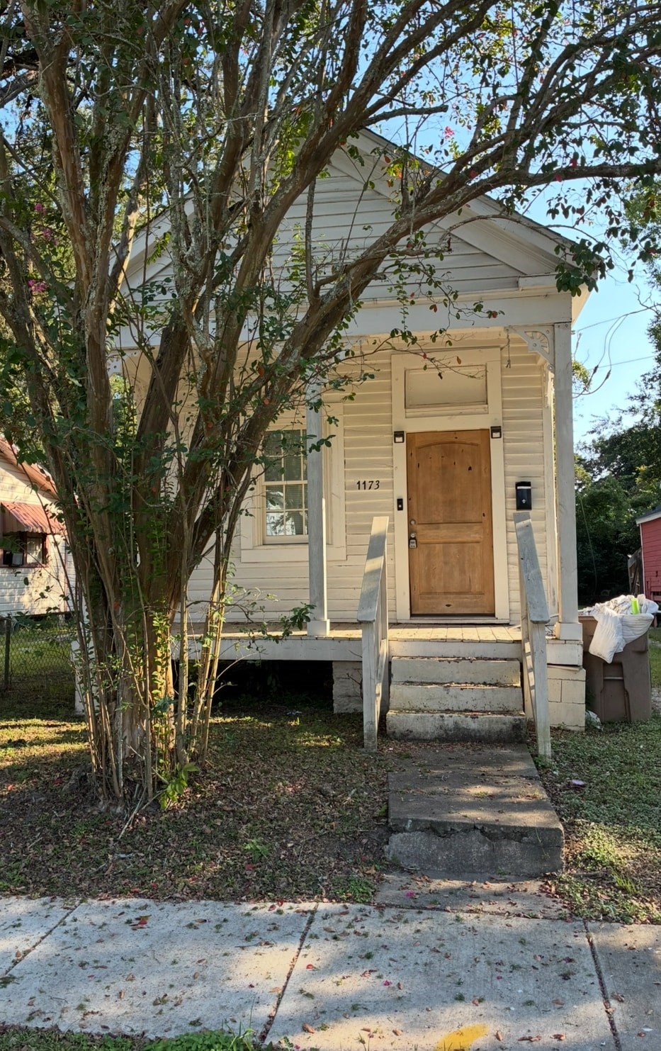 A small white house with a brown door and a tree in front.