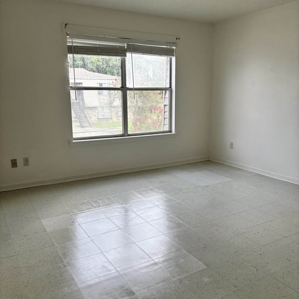 an empty living room with a window and tiled floors