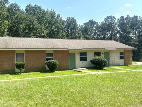 a brick house with a grassy yard and trees in the background