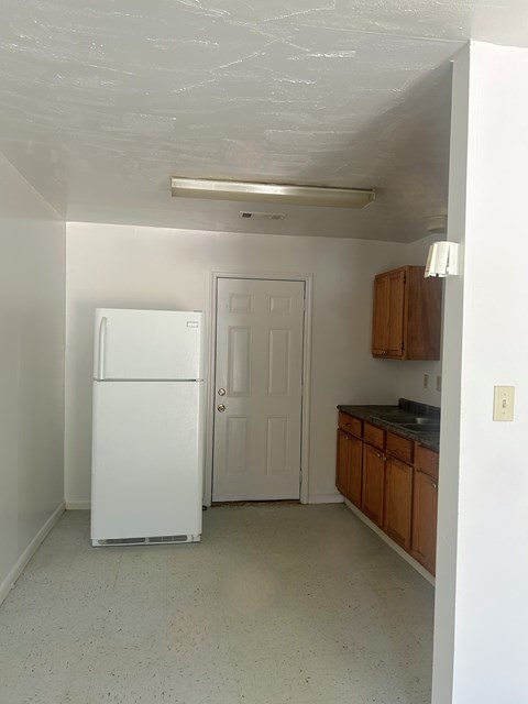 an empty kitchen with a white refrigerator and a door