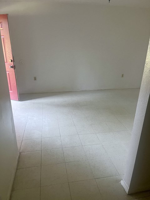an empty room with a white tiled floor and a pink door