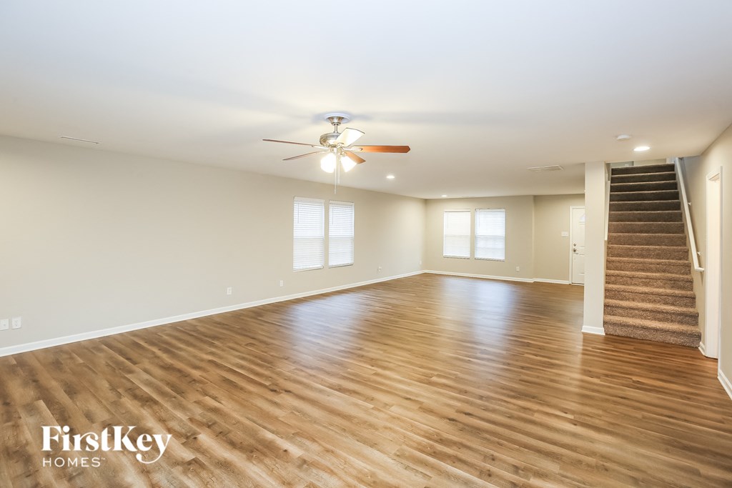 A spacious room with wooden floors and a staircase on the right side.
