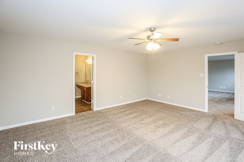 A carpeted room with a ceiling fan and two doors.