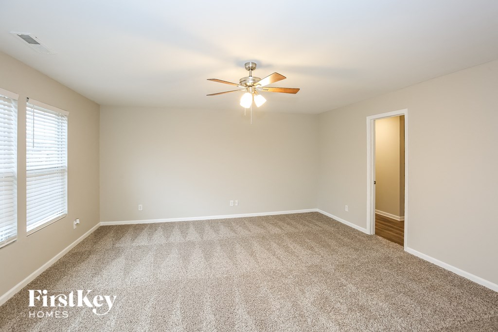 A spacious room with a carpeted floor and a ceiling fan.