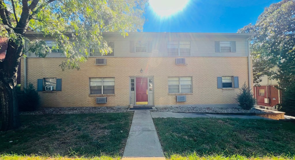 a yellow brick building with a red door and a sidewalk in front of it