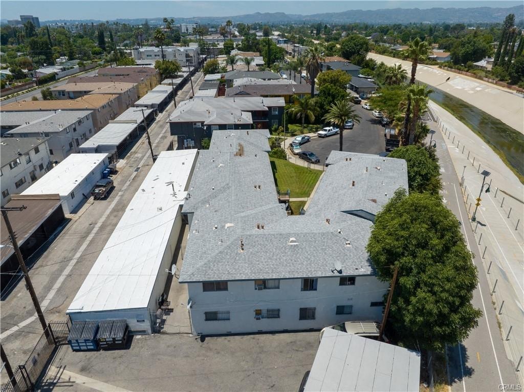 A large white building with a grey roof is surrounded by other buildings and palm trees.