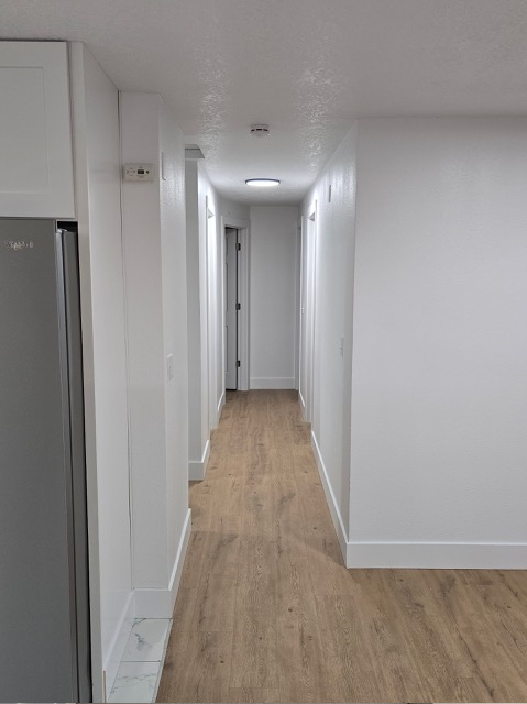 A long hallway with a refrigerator on the left and a door at the end.