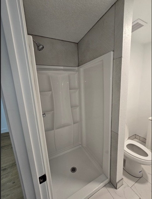 A white bathroom with a toilet and a walk in shower.