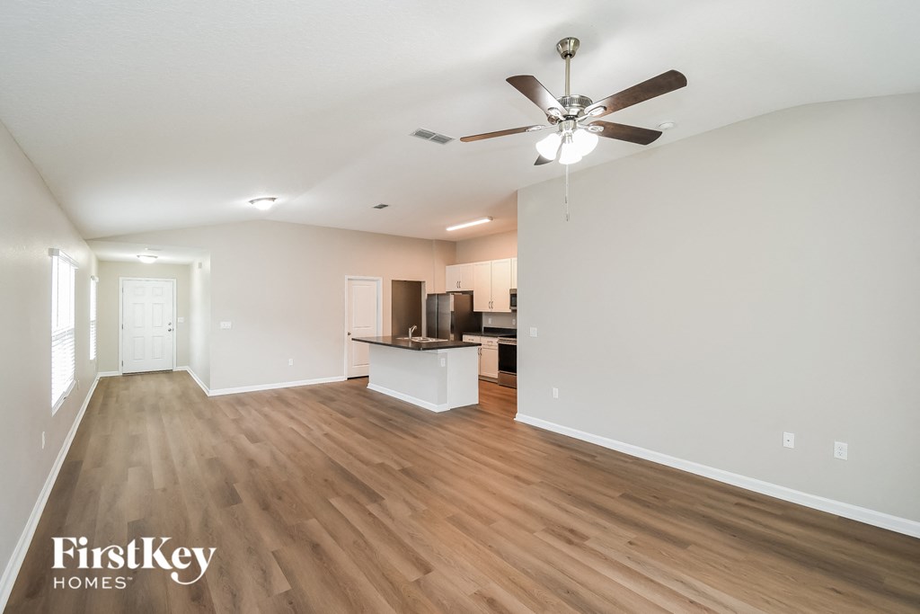 an empty living room with a ceiling fan and a kitchen