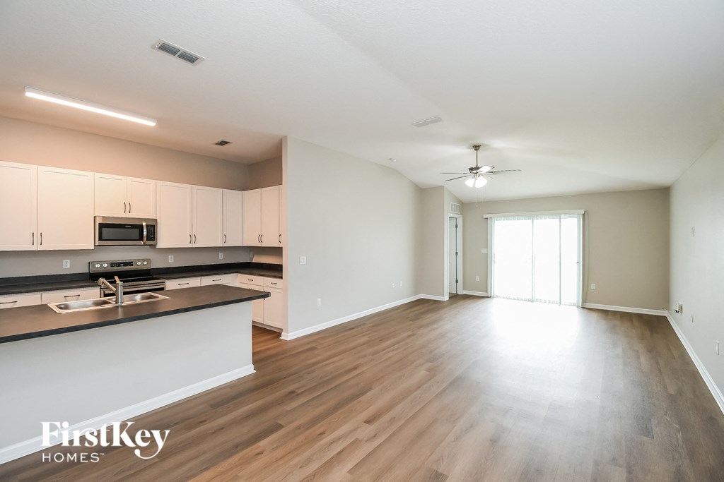 an empty kitchen and living room with white cabinets and wood flooring