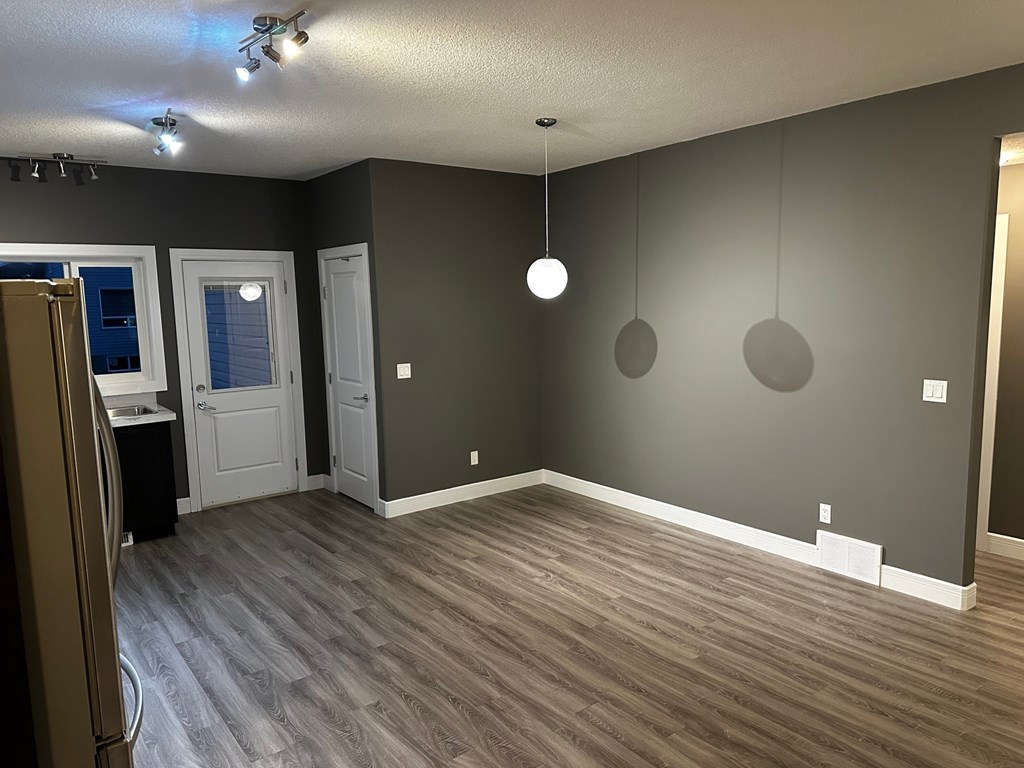 A room with a refrigerator on the left and a wooden floor.