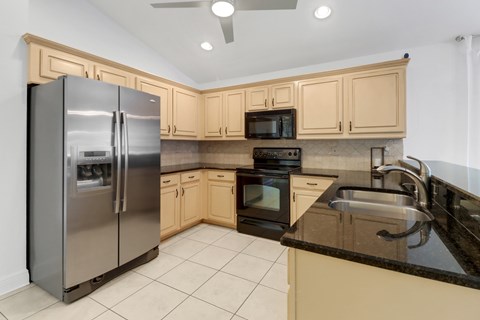 A kitchen with a black counter top and a stainless steel refrigerator.