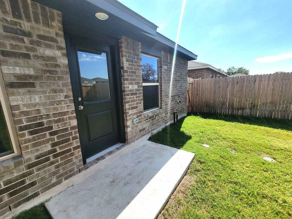 a front door of a brick house with a lawn and a fence