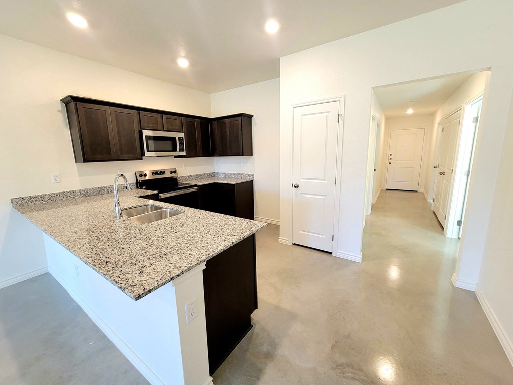 an empty kitchen with granite counter tops and a long hallway