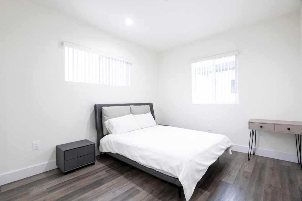 a bedroom with a bed and a desk and two windows