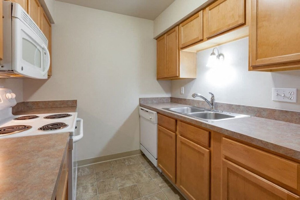 A kitchen with a white stove top oven, a white dishwasher, and wooden cabinets.