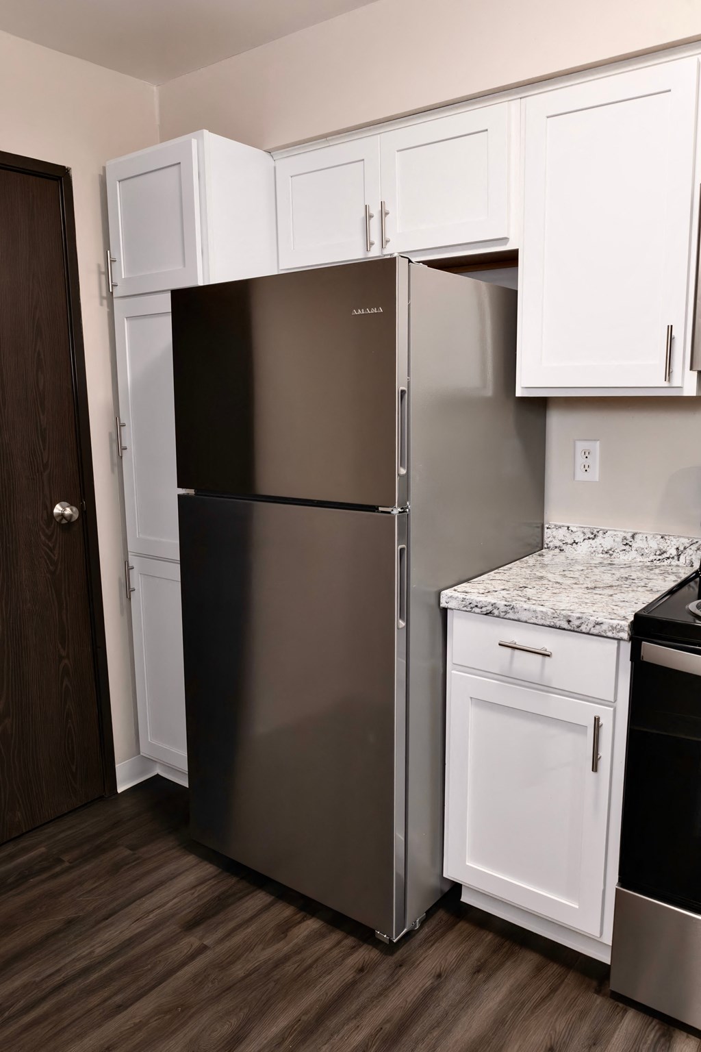 A stainless steel refrigerator with white cabinets above it.