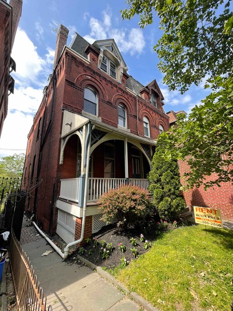 A red brick building with a balcony and a sign that says "RENT".