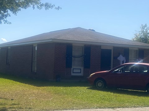 A red car is parked in front of a brick house.