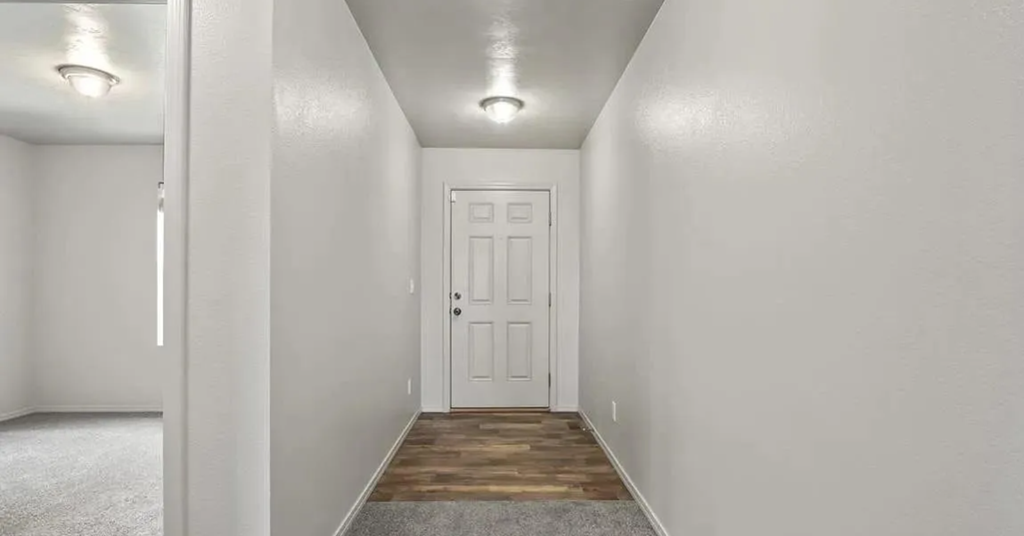 a white room with a white door and a hallway with a wooden floor