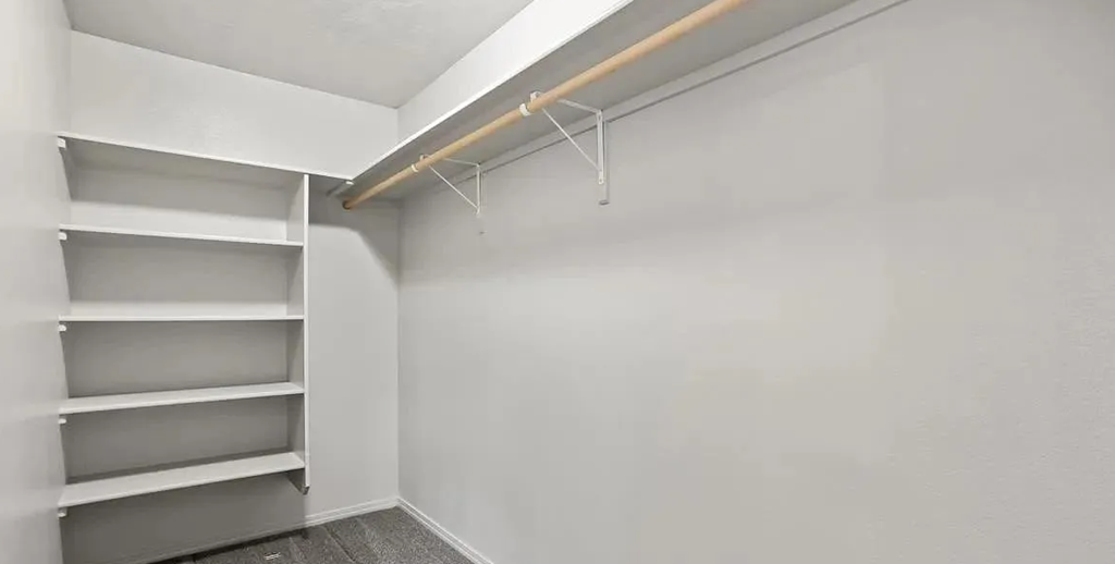 a walk in closet in a white room with shelves and