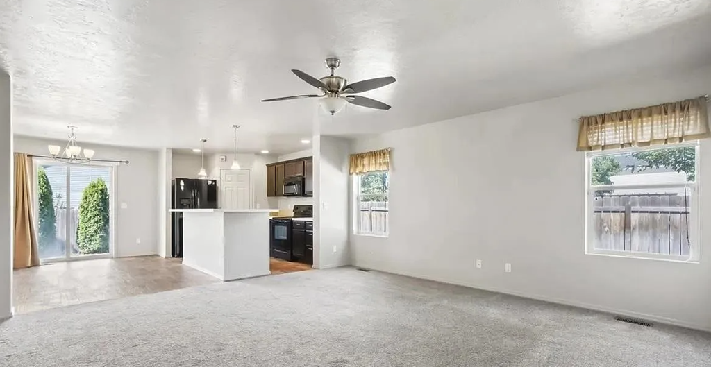 an empty living room with a kitchen and a ceiling fan
