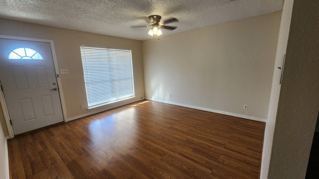 an empty living room with wood floors and a ceiling fan